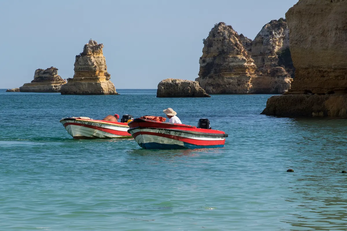 Dois barcos de pesca parados em água turquesa, junto a falésias calcárias.